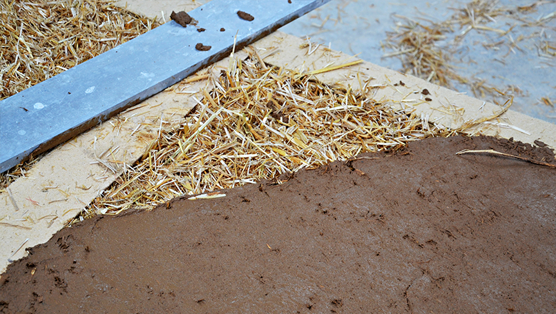 Das festgestampfte Stroh wird mit einer Lehmschicht bedeckt